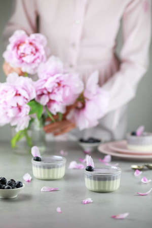 Homemade Italian dessert panna cotta with blue berries and bouquet of peony flowers on gray background.の写真素材