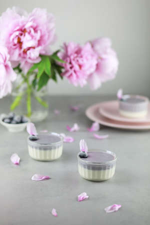 Homemade Italian dessert panna cotta with blue berries and bouquet of peony flowers on gray background.の写真素材