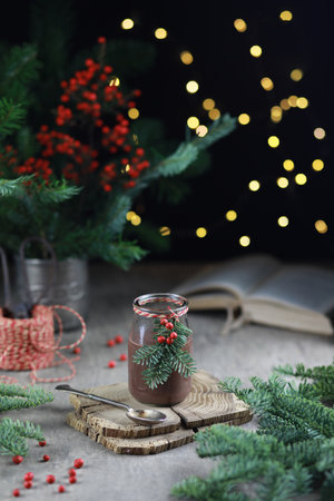 Hot chocolate in glass jar decorated with fir and red berries on festive rustic background.の写真素材
