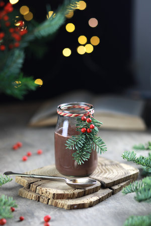 Hot chocolate in glass jar decorated with fir and red berries on festive rustic background.の写真素材