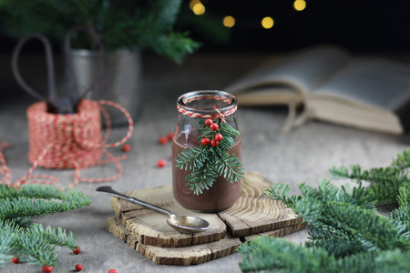 Hot chocolate in glass jar decorated with fir and red berries on festive rustic background.の写真素材