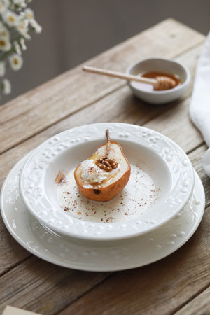 Honey baked pear with ice cream, walnuts, cinnamon, spices with sauce on white plate on wooden table.の写真素材