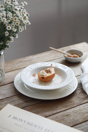 Honey baked pear with ice cream, walnuts, cinnamon, spices with sauce on white plate on wooden table.の写真素材