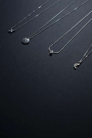 Silver pendants, chains on black background - minimal jewelery flat layの写真素材