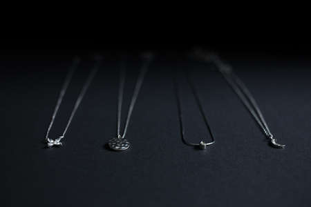 Silver pendants, chains on black background - minimal jewelery flat layの写真素材