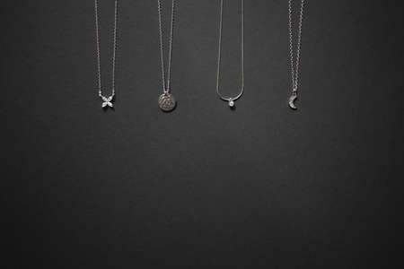 Silver pendants, chains on black background - minimal jewelery flat lay