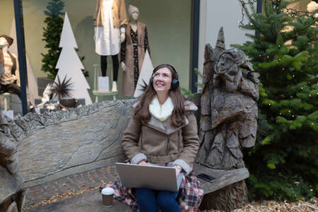 Young woman is sitting on the bench with the laptop and wearing headphonesの写真素材