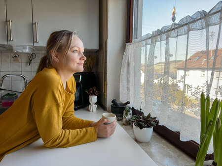 Woman is holding a cup whilst watching out of the window