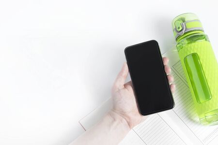 One bright green fitness sport bottle or flask with dispenser and filled with water. Smartphone...
