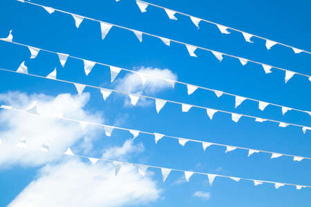 White bunting pennant triangle flags hanging on rope line in many rows. Bright blue sunny summer sky on the background. Freedom or peace concept. Postcard or calendar format with empty space for text.の写真素材