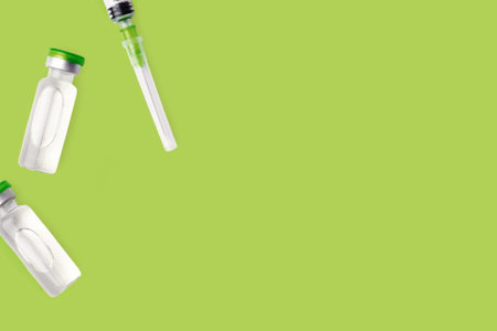 Vaccine Bottles And Needle Syringe On Green Background.  Pharmaceutical Glass Vials Containers....