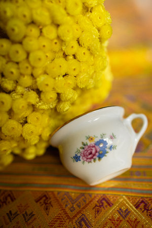 A small white coffee cup with flower design on table near yellow flowersの写真素材