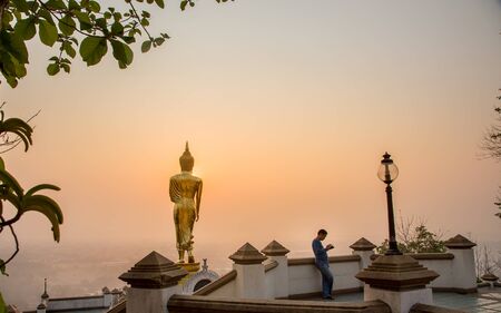 Nan, Thailand - April 25, 2016: An unidentified man stands alone to play phone Buddha Mountain Wat Khao Noi during sunset on the background Lifestyle concept outdoor trips in Nan, Thailand - April 25, 2016のeditorial素材
