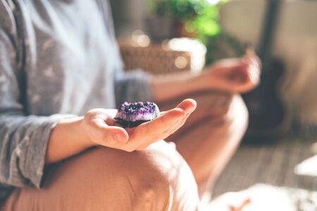 Young beautiful woman is meditating with a crystal quartz in her hand. Sits on the floor at home.の写真素材