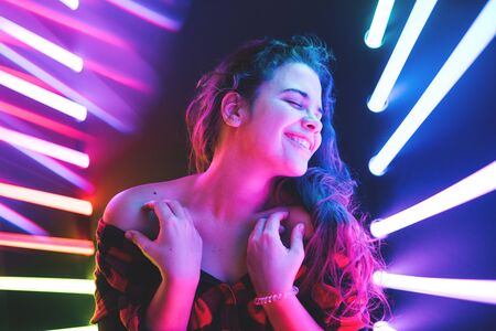 Cheerful cute smiling curly girl at neon violet background in a plaid shirt with bare shoulder.の写真素材