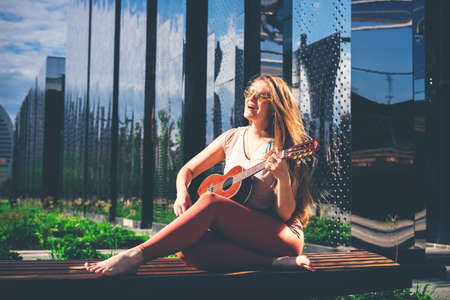 Young pretty woman playing her ukulele outdoors sitting in the modern park and smiling. Concept...