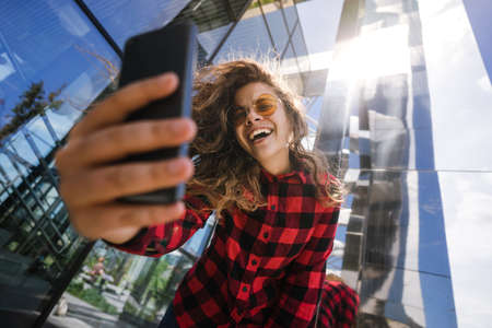 Portret of smiling girl making selfie with smart phone outdoors on the city street. Taking self...