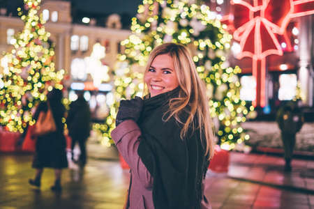 Young beautiful girl laughs on a christmas background with garlands in the city.