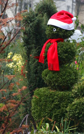 Bush cut to shape of a snowman wearing a red cap and scarfの写真素材
