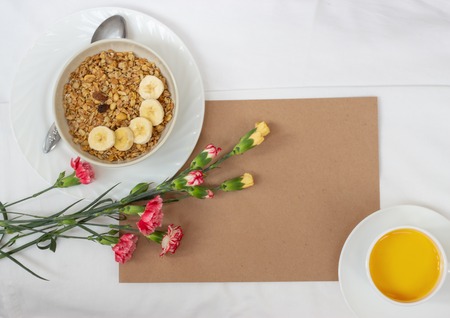 Breakfast in bed with muesli, fruit and orange juice with flowers and a card