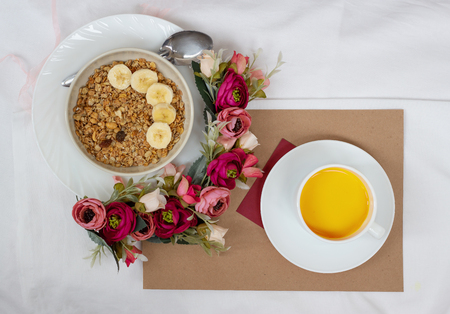 Breakfast in bed with muesli, fruit and orange juice with flowers and a cardの写真素材