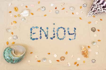 Sand on the beach in summer, the inscription enjoy from the shells on the sand. Close-up. Flat lay. Top viewの写真素材