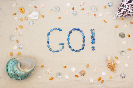 Sand on the beach in summer, the inscription go! from the shells on the sand. Close-up. Flat lay. Top viewの写真素材