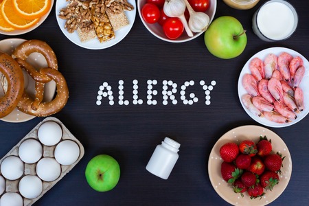 Allergy food concept. Allergy food as milk, oranges, tomatoes, garlic, shrimp, peanuts, eggs, apples and bread and strawberries on wooden tableの写真素材
