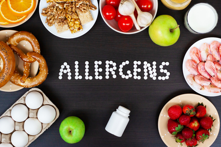 Food allergens as milk, oranges, tomatoes, garlic, shrimp, peanuts, eggs, apples and bread and strawberries on wooden table. Inscription food allergens.の写真素材