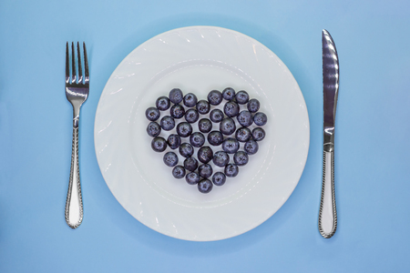 Heart of blueberries on white plate with cutlery. Love vegan diet concept. Valentine's Day. Top viewの写真素材