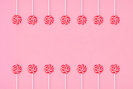 Many colorful lollipop candys arranged in two group and empty space in the center on pink background. Flat lay concept.の写真素材