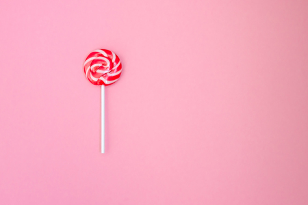 Lollipop. Striped lollipop on a gently pink background. Red and white stripes on the candy. Flat lay. Top viewの写真素材