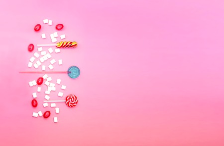 Flat lay composition with yummy lollipops and marshmallows and space for text on pink background. Different sweets. Copy spaceの写真素材