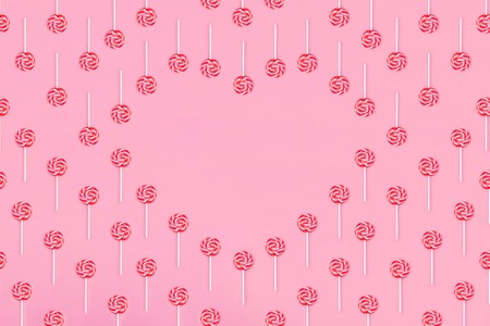 Heart made out of lollypop candies on pink background, copy space. Sweet childhood concept. Valentine's Day greeting card. Flat Lay.の写真素材
