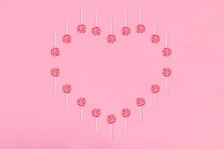 Heart made out of lollypop candies on pink background, copy space. Sweet childhood concept. Valentine's Day greeting card. Flat Lay.の写真素材