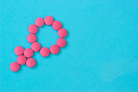 Medicine for woman. Menopause, pms, menstruation or estrogen concept. Female health. Gender symbol made from pink red pills or tablets on blue background. Copy spaceの写真素材