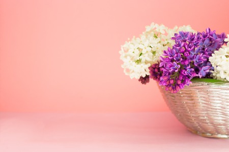 basket with a branch of white and purple lilac flowers on a coral pink background. Copy space. Beautiful summer bouquet.の写真素材