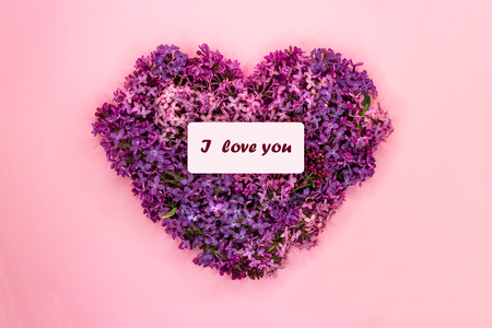 Heart shape made of purple lilac flowers with inscription I love you on pastel pink background. Love symbol. Copy space. Top view. Greeting cardの写真素材