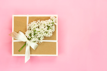 Gift box with holiday bow and white lilac flowers and green leaves on light pink background. Copy space. Top view.の写真素材