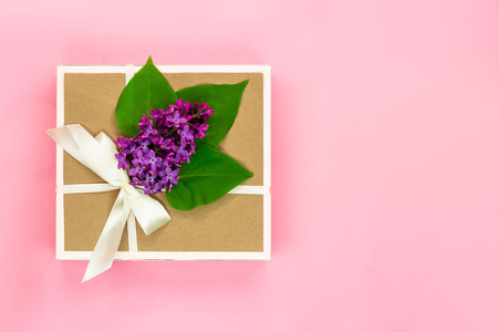 Gift box with holiday bow and violet lilac flowers and green leaves on light pink background. Copy space. Top view.の写真素材