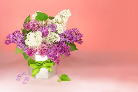 Bouquet white and purple lilac flowers in vase in a vase with a gift bow on table, copy space. PInk background. Festive flowers.の写真素材