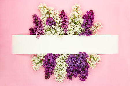 Festive invitation or greeting card with beautiful floral border. Violet and white syringa flowers on light pink background. Copy space. Top view.の写真素材