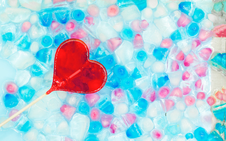 One candy heart shape against the background of transparent, white, pink and blue ice cubes. Fresh summer pattern with copy space. Top view. Flat lay.の写真素材