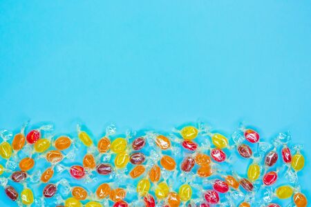 Bright multicolored candies in wrappers of transparent mica, sweets on blue background, colorful candy scattered, top view with copy space. Flat layの写真素材