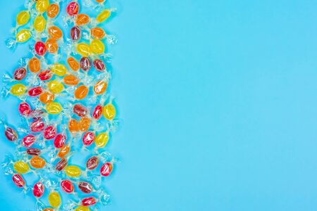 Bright multicolored candies in wrappers of transparent mica, sweets on blue background, colorful candy scattered, top view with copy space. Flat layの写真素材