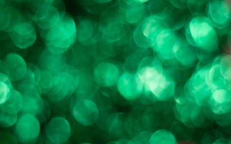 Green bokeh on a dark background. Green glitter abstract background with bokeh defocused lights.の写真素材