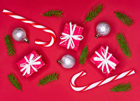 Christmas composition. Christmas decorations, fir tree branches, giftboxes and candycanes on red...