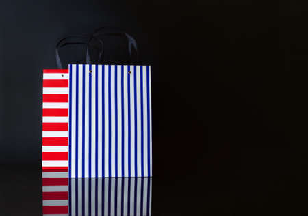 White, blue and red striped paper shopping bag on black background. Black Friday sale shopping.の写真素材