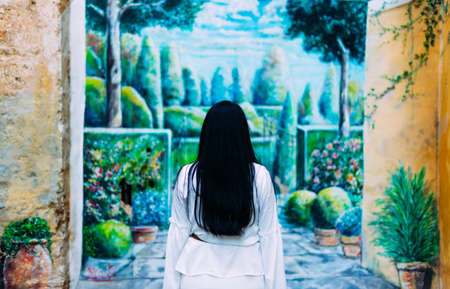 Brunette woman with long hair dressed in white with her back to a wall-painted garden mural. art conceptの写真素材