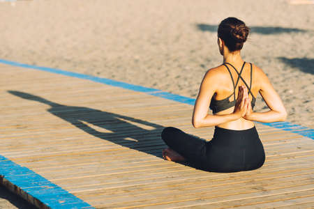 young woman doing yoga exercise on the ground outdoors by the sea at sunsetの写真素材